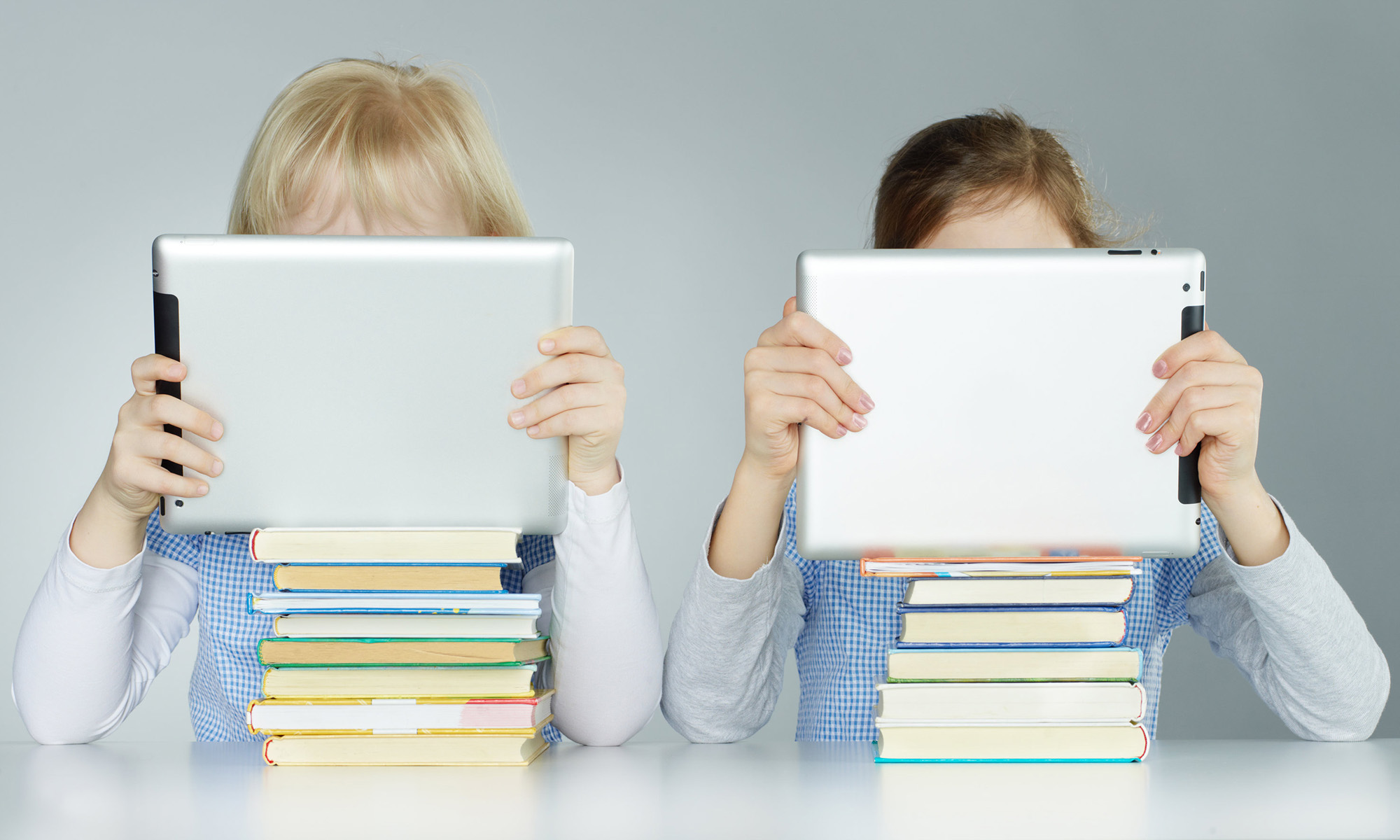 Two pupils leaning on a pile of books while reading on touchpad